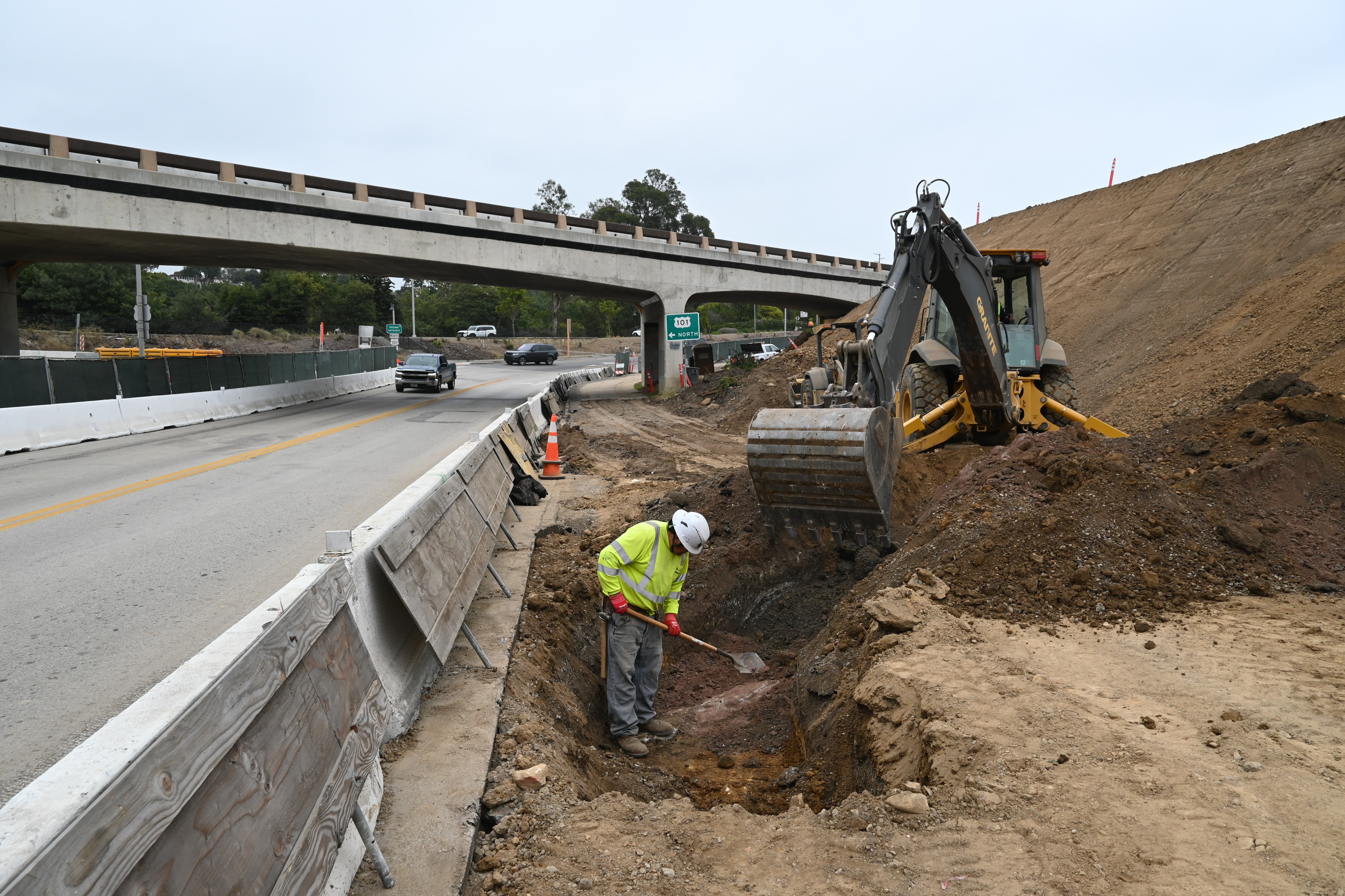 Worker and construction equipment digging on roadside